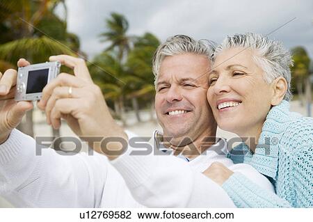 Stock Image - A senior couple on a beach taking a picture with a digital camera. Fotosearch