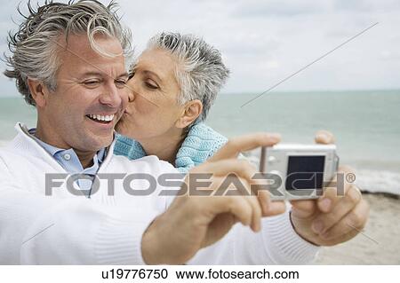 Stock Image - A senior couple on a beach taking a picture with a digital camera. Fotosearch