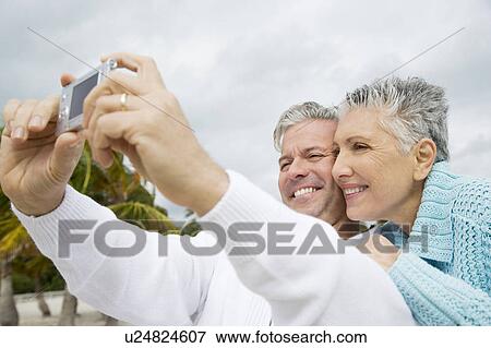 A senior couple on a beach taking a picture with a digital camera View Large Photo Image Stock Photo - A senior couple on a beach taking a picture with a digital camera. Fotosearch