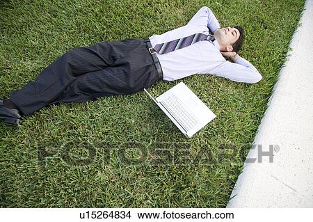 Picture - A businessman laying in a park with his laptop. Fotosearch