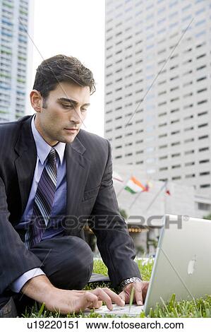 Stock Image - A businessman sitting in a park with his laptop. Fotosearch
