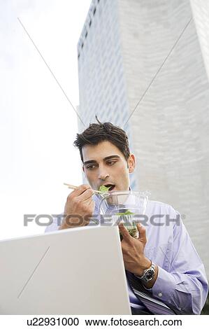 A businessman using a laptop and eating his lunch View Large Photo Image Stock Image - A businessman using a laptop and eating his lunch. Fotosearch