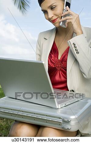 Stock Image - A businesswoman talking on a mobile phone using a laptop computer. Fotosearch