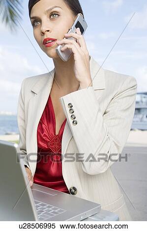 A businesswoman talking on a mobile phone using a laptop computer View Large Photo Image Stock Photography - A businesswoman talking on a mobile phone using a laptop computer. Fotosearch