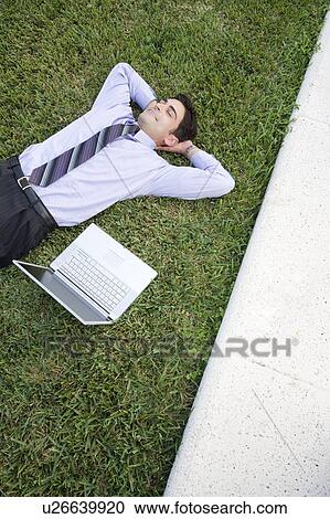 A businessman laying in a park with his laptop View Large Photo Image Stock Image - A businessman laying in a park with his laptop. Fotosearch