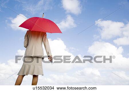 A businesswoman standing underneath an umbrella holding a mobile phone View Large Photo Image Picture - A businesswoman standing underneath an umbrella holding a mobile phone. Fotosearch