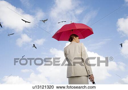 Stock Image - A businesswoman standing underneath an umbrella. Fotosearch