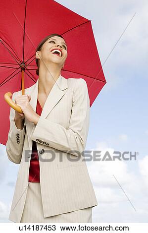 Stock Image - A businesswoman standing underneath an umbrella. Fotosearch