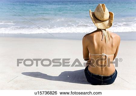 Stock Photograph - A young woman sitting on the beach. Fotosearch