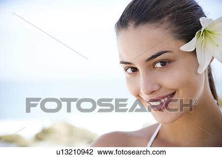 Stock Image - Portrait young Hispanic woman with flower in hair. Fotosearch