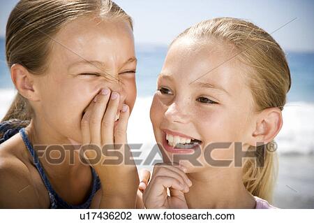 Stock Image - A young girl whispering to her friend on the beach. Fotosearch