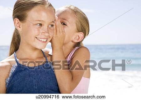 A young girl whispering to her friend on the beach View Large Photo Image Stock Photograph - A young girl whispering to her friend on the beach. Fotosearch