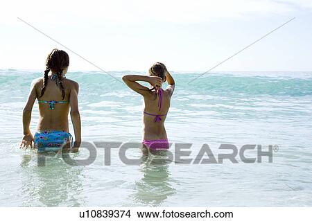 Picture - Two young girls standing in the sea. Fotosearch