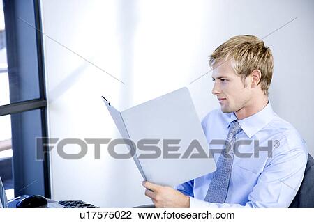 Stock Image - Businessman reading documents whilst seated in his office. Fotosearch