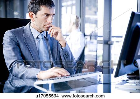 Picture - Businessman sat at a desk using a computer looking stressed. Fotosearch
