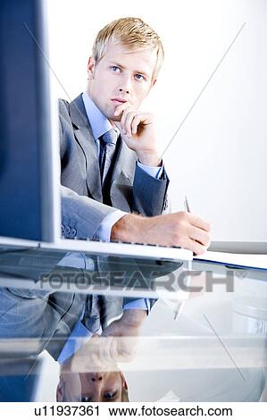 Stock Image - Businessman writing whilst seated at a desk in a modern office building. Fotosearch