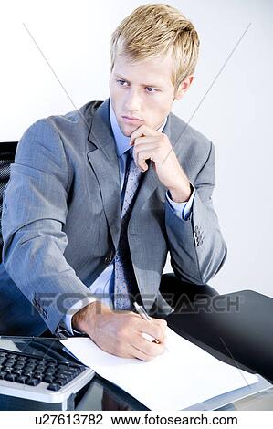 Businessman writing whilst seated at a desk in a modern office building View Large Photo Image Stock Image - Businessman writing whilst seated at a desk in a modern office building. Fotosearch