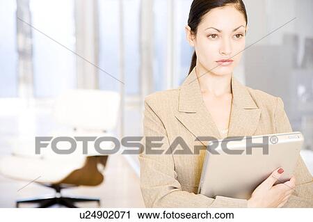 Stock Image - Businesswoman looking serious whilst clutching her laptop. Fotosearch