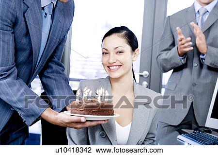 Stock Image - Colleagues celebrating a businesswoman's birthday with a cake. Fotosearch