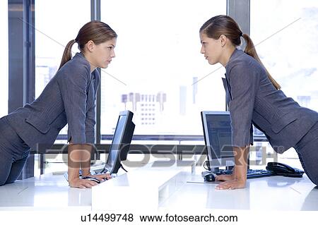 Stock Photo - Identical female twins looking at each other over an office desk with computers. Fotosearch