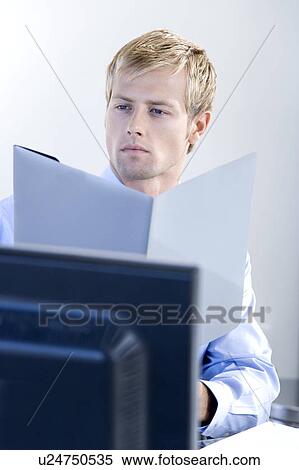 Man reading documents whilst seated in his office View Large Photo Image Stock Photography - Man reading documents whilst seated in his office. Fotosearch