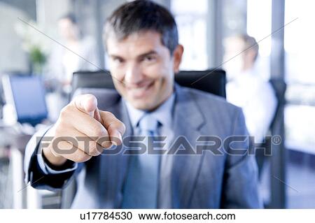 Smiling businessman pointing towards camera View Large Photo Image Stock Image - Smiling businessman pointing towards camera. Fotosearch