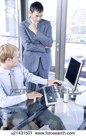 Two businessmen in an office looking at a computer screen View Large Photo Image Stock Image - Two businessmen in an office looking at a computer screen. Fotosearch