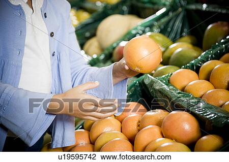 Stock Image - Cropped image of a girl selecting grapefruits in a supermarket.. Fotosearch