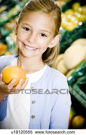 Stock Photography - Portrait of a young girl holding a grapefruit in a supermarket. Fotosearch