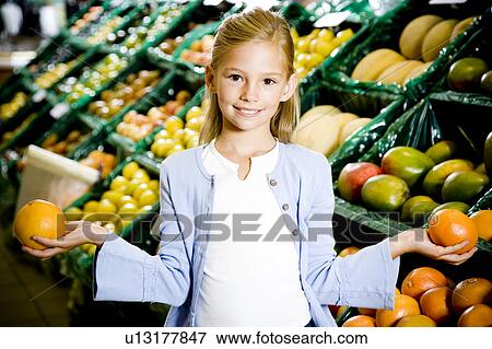 Stock Photo - Portrait of a young girl holding two grapefruits in a supermarket. Fotosearch