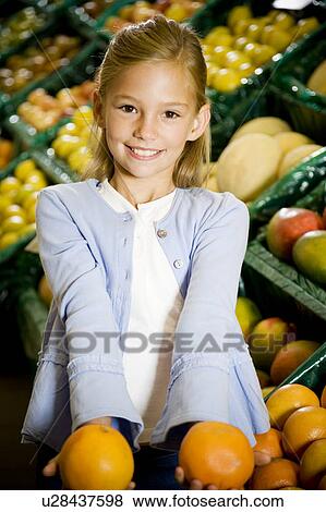 Stock Photo - Portrait of a young girl holding two grapefruits in a supermarket. Fotosearch
