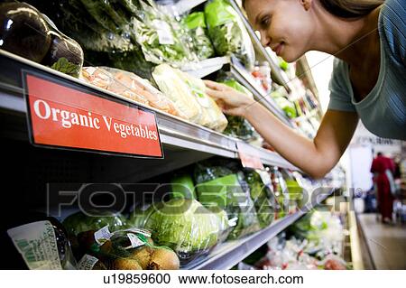 Stock Image - Woman reading the label on an organic food packaging in a supermarket. Fotosearch