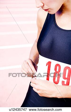 Stock Photo - Close in crop of a female athlete attaching her competitors number. Fotosearch