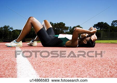 Stock Image - Female athlete resting on a running track. Fotosearch