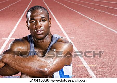 Stock Photograph - Portrait of a male athlete resting sitting on a running track. Fotosearch