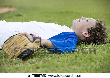 Stock Image - Boy laying down on the grass after a baseball game. Fotosearch