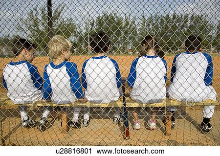 Stock Image - Rear view little league baseball team sitting on bench. Fotosearch