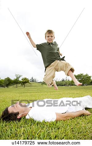 Stock Photography - Boy jumping over man lying on grass. Fotosearch