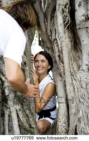 Stock Photo - Couple playing hide and seek round a tree. Fotosearch