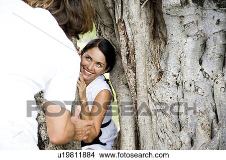 Picture - Couple playing hide and seek through a hollow tree. Fotosearch