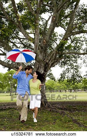 Stock Image - couple with umbrella walking in the park. Fotosearch