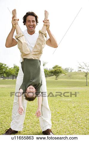 Stock Image - father holding son upside down in the park. Fotosearch