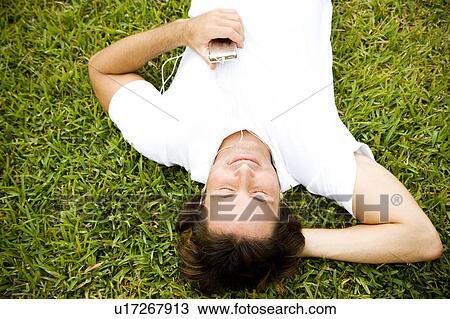 Man lying on the grass listening to personal stereo View Large Photo Image Stock Image - Man lying on the grass listening to personal stereo. Fotosearch