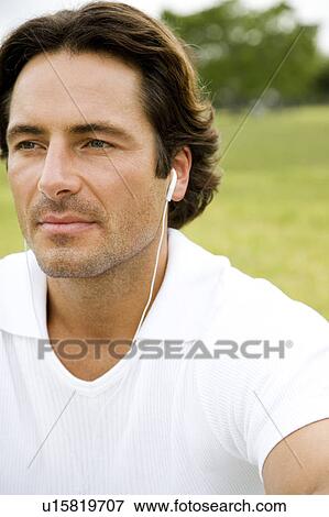 Stock Photo - Portrait man with earphones sitting in the park. Fotosearch