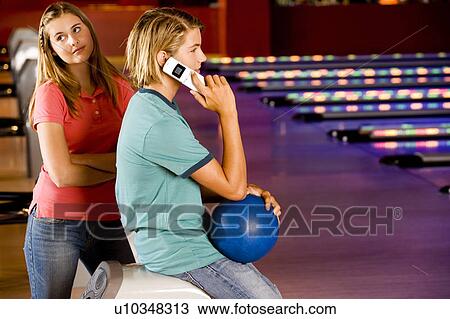 Stock Image - Teenage boy and girl in a bowling alley, boy talking on mobile phone. Fotosearch
