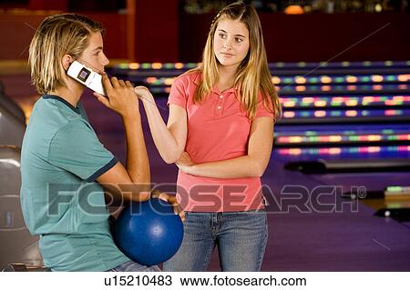 Stock Image - Teenage boy and girl in a bowling alley, boy talking on mobile phone. Fotosearch