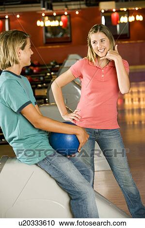 Stock Image - Teenage boy and girl in a bowling alley, flirting and exchanging phone numbers. Fotosearch
