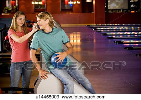 Stock Photo - Teenage boy and girl in a bowling alley, talking on mobile phone. Fotosearch