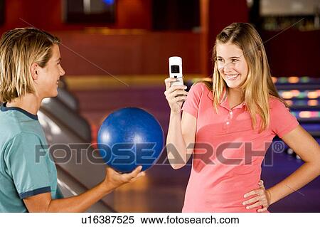 Stock Photography - Teenage boy and girl in a bowling alley, girl taking a picture. Fotosearch