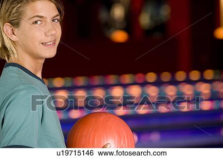 Stock Photograph - Teenage boy in a bowling alley, holding a red bowling ball. Fotosearch